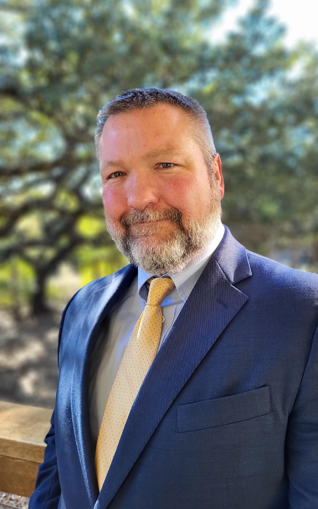 Headshot of Michael Dennis against trees outside 