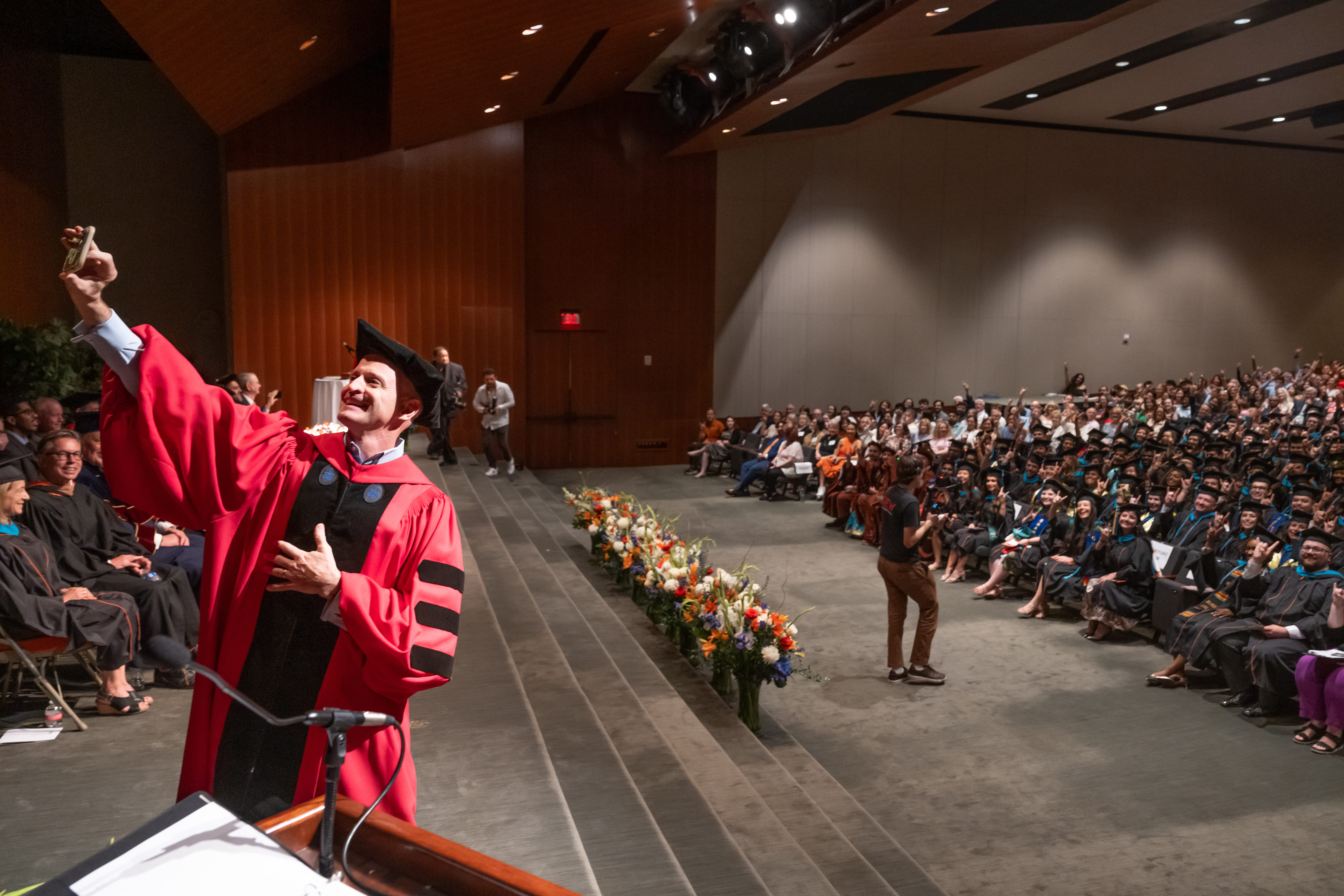 Dean JR DeShazo captures a full LBJ Auditorium with a selfie during the 2024 graduation ceremony.