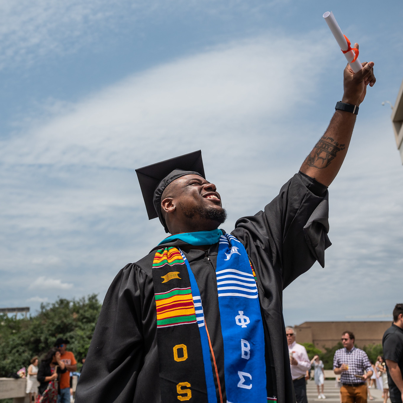 An LBJ student graduating and waving his diploma on the plaza