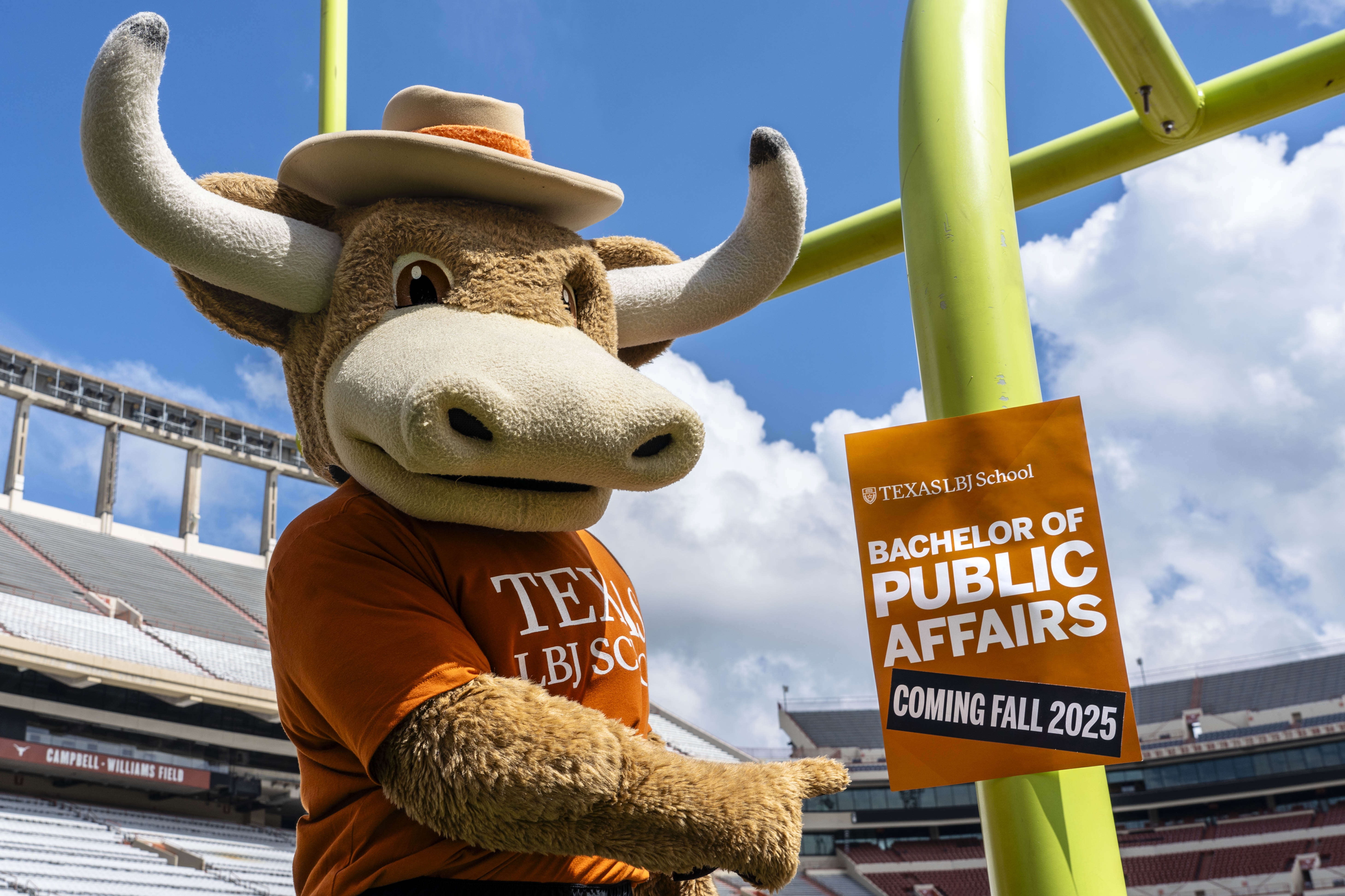 Hookem the mascot with a sign for the undergraduate degree on the football field.
