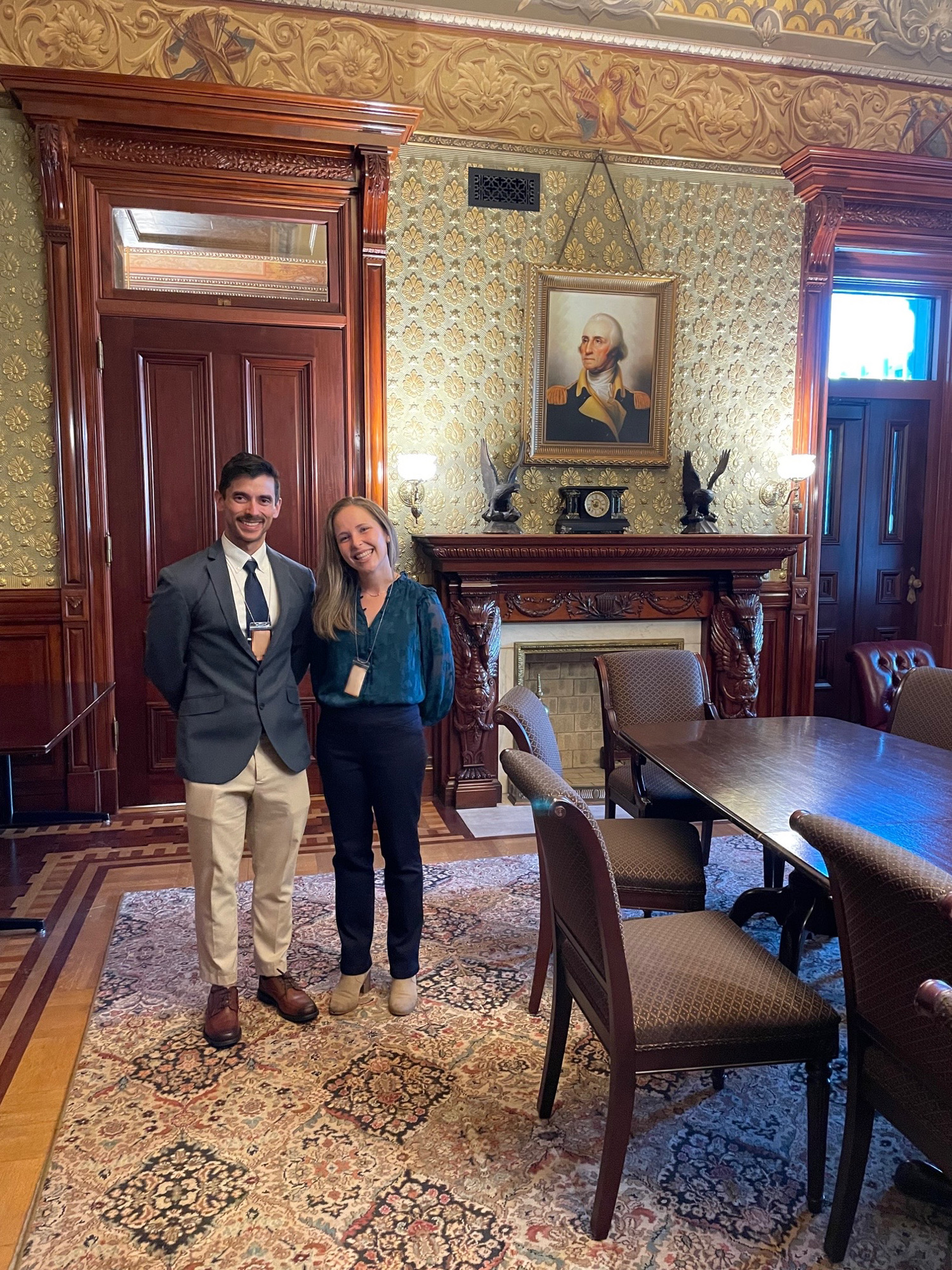 Two LBJ students in business attire stand smiling in a decorated White House room
