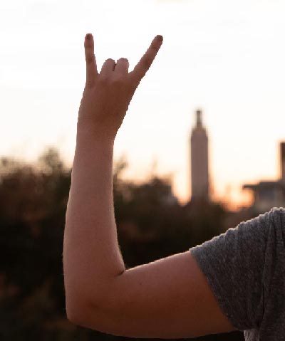 An LBJ student gives the "Hook 'em" sign with the UT Tower in the background at Gone To Texas 2018