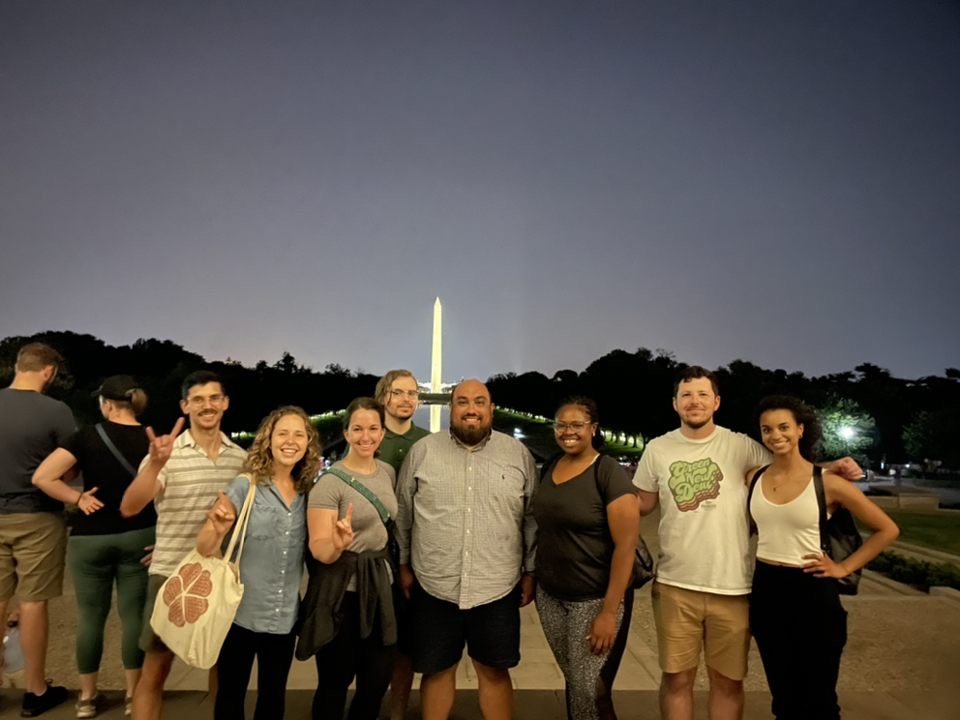 Group of students pose smiling in front of Washington Monument at night 