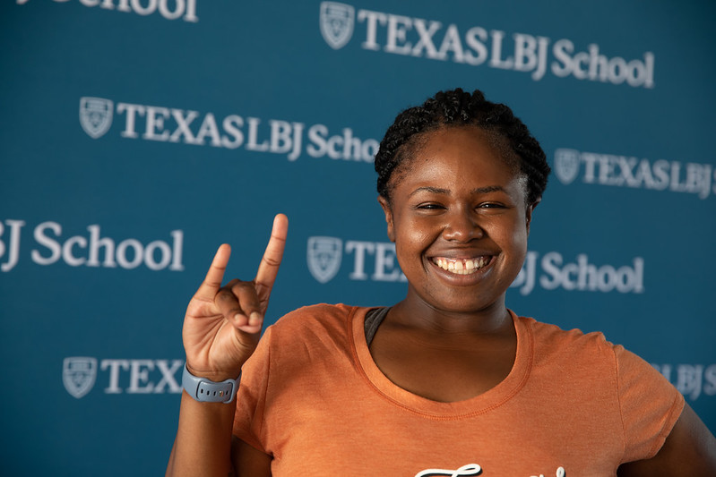LBJ Student pictured in front of branded step and repeat, throwing horns up 
