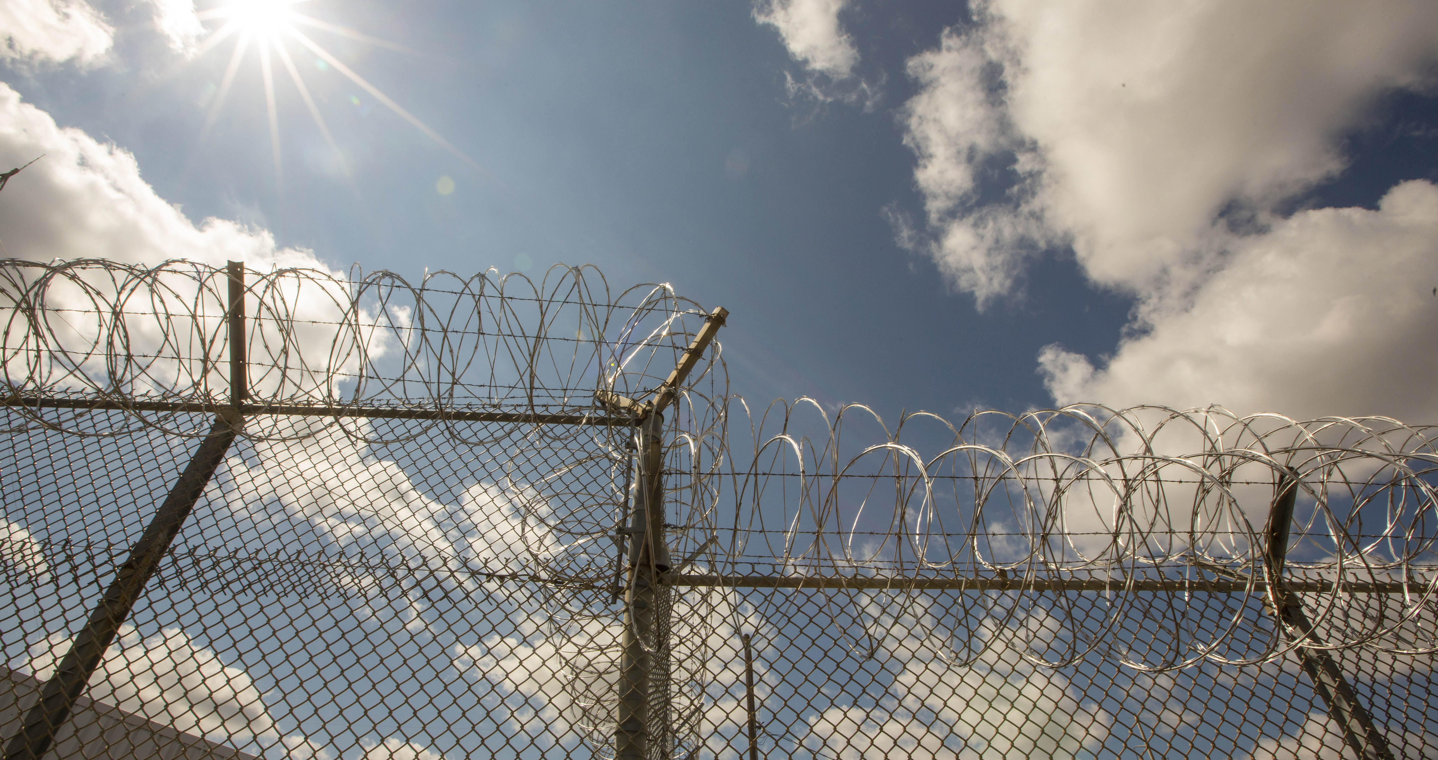 Barbed wire on top of a prison fence with a background of a blue sky and sunshine