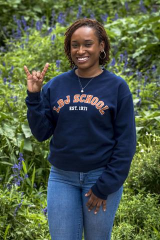 Morgan Brown wearing an LBJ School sweatshirt with a hookem hand sign.