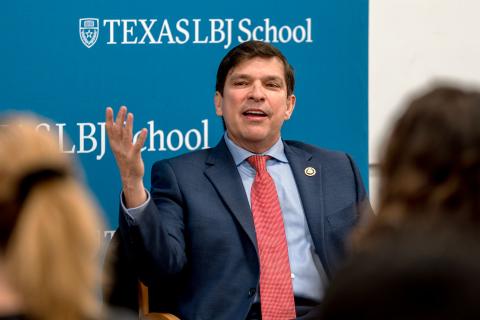 Vicente Gonzales speaking in front on LBJ School step and repeat banner