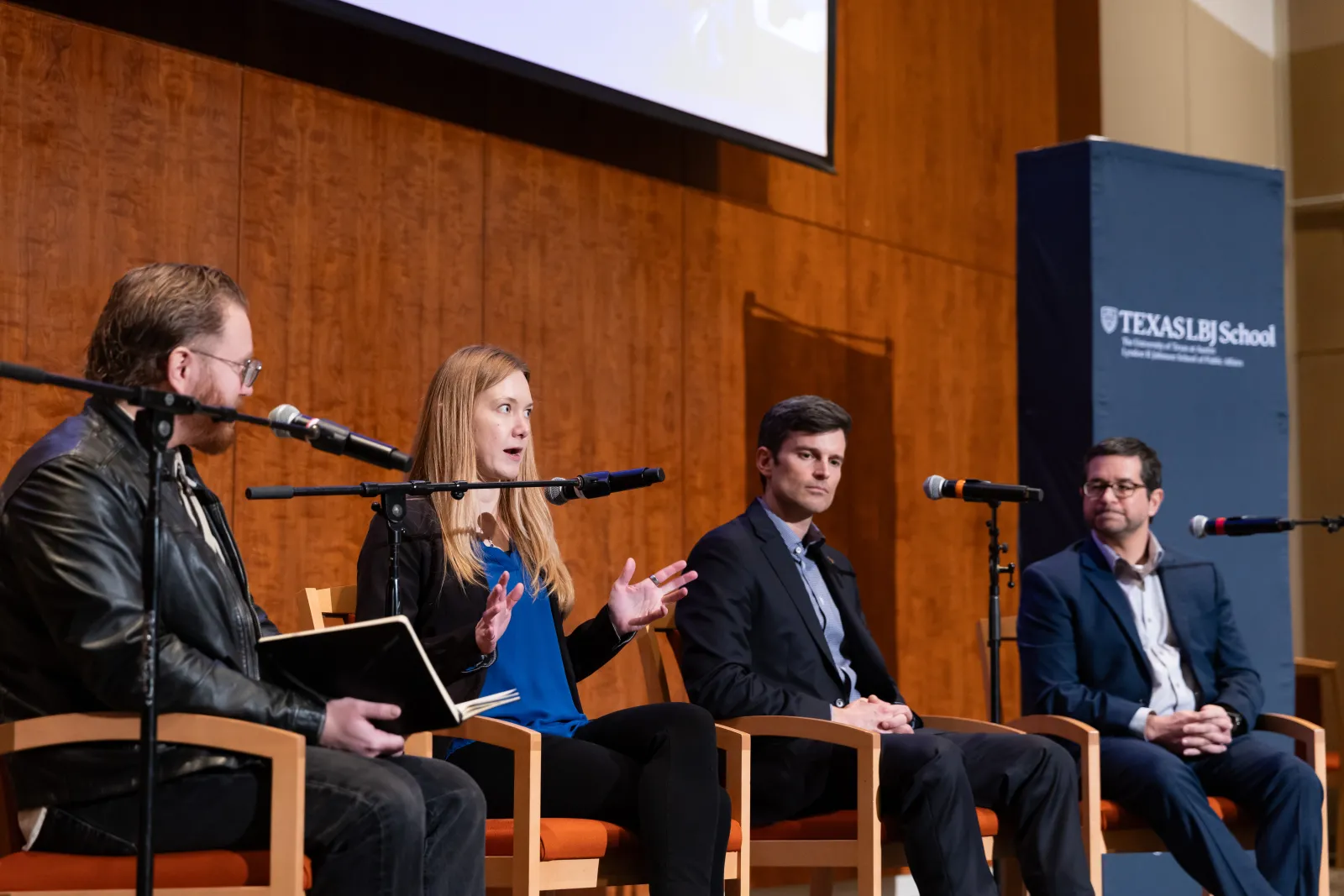 3 men and a woman speaking in front of mics