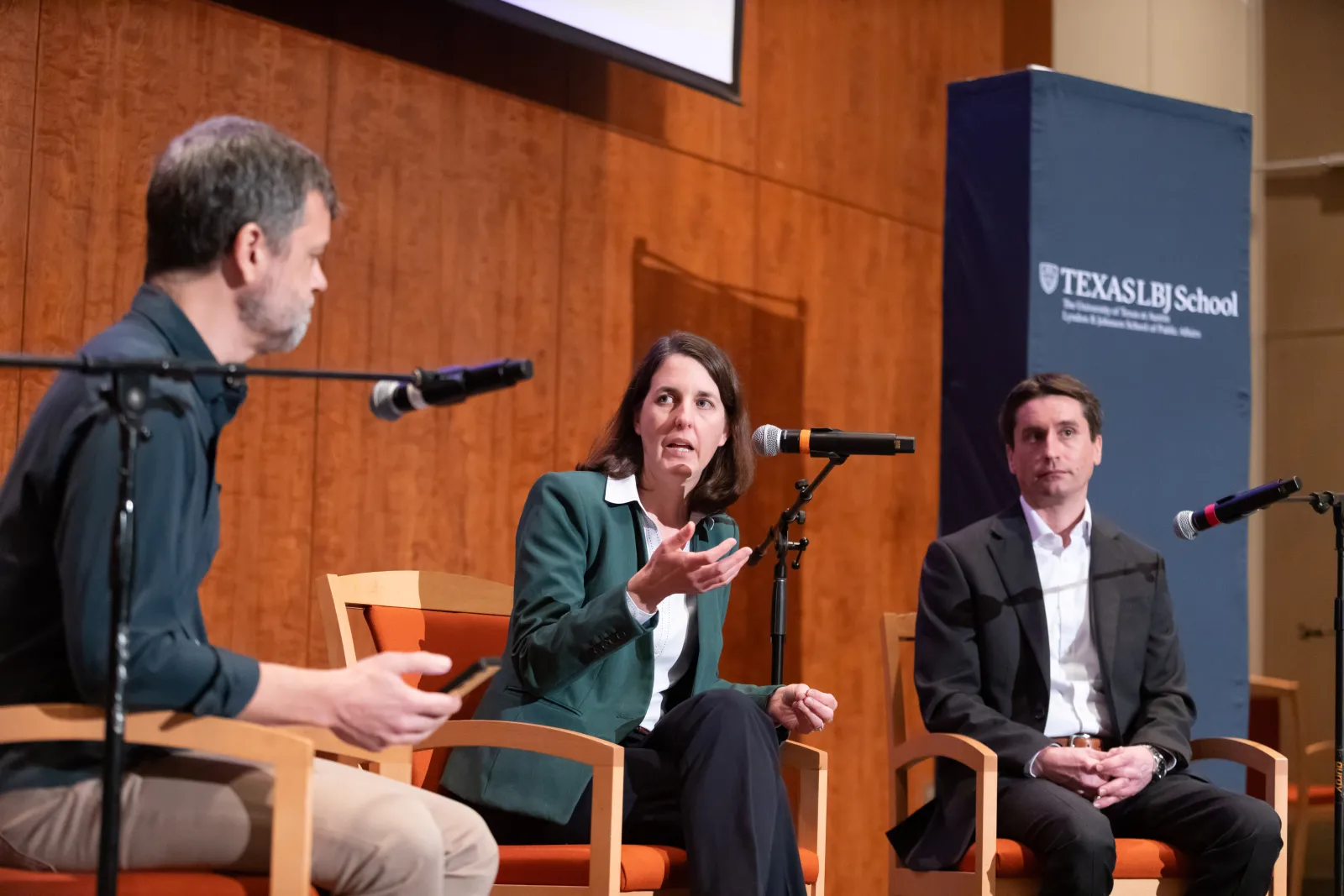 2 men and a woman speaking to each other in front of microphones