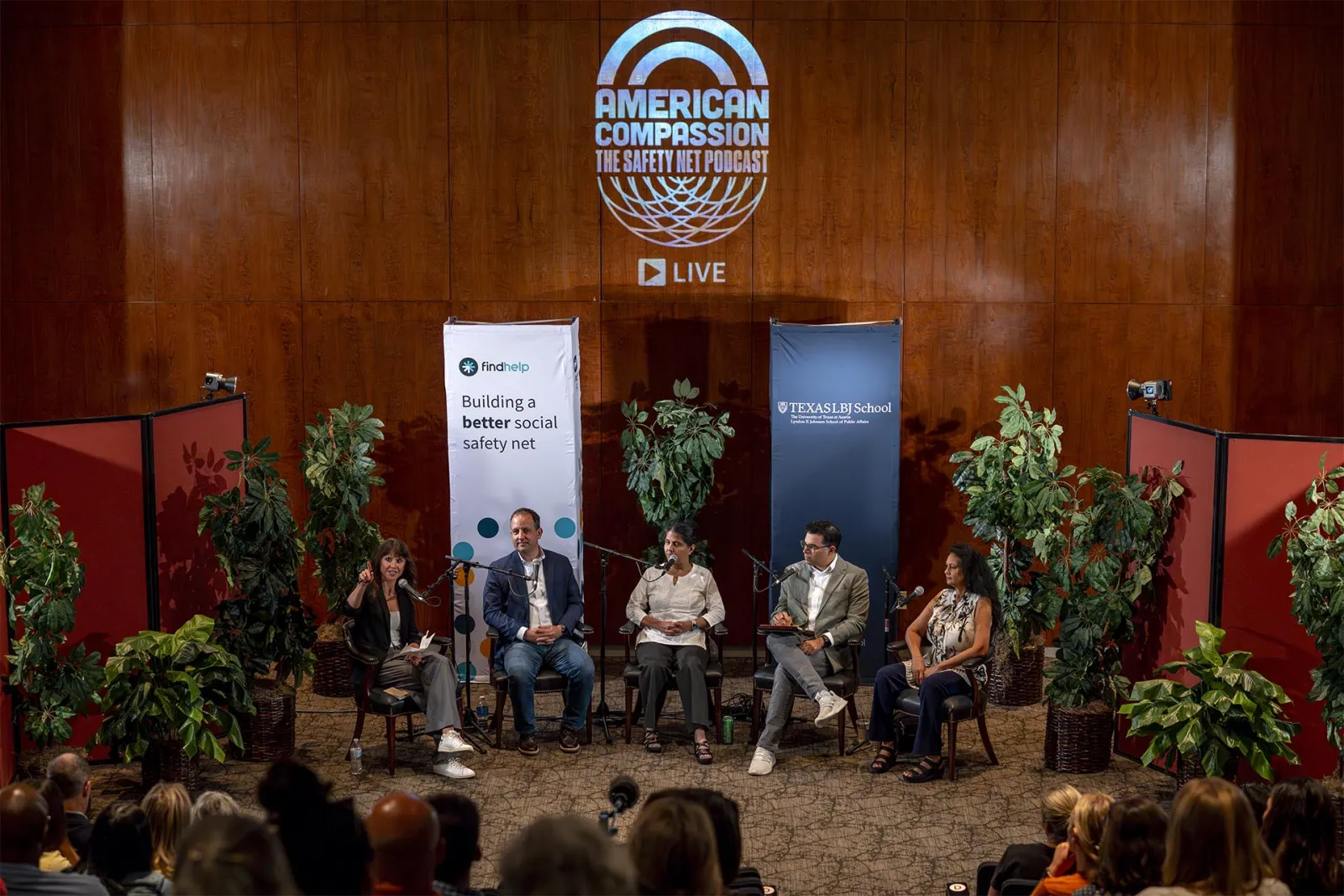 3 women and 2 men sitting in front of an auditorium crowd, speaking into microphones, with the words "American Compassion" projected on to the wall