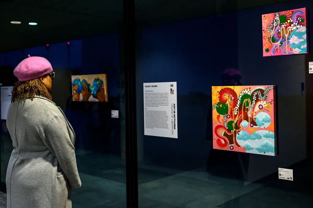 woman in pink hat looking at art works affixed to a glass windom