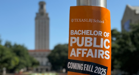 A burnt orange poster of the Undergrad Public Affairs degree sits in front of the UT Tower.