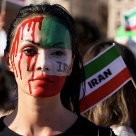Protester with Iranian flag painted on one side of face and fake blood on the other