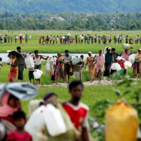The image shows refugees walking across a field. 