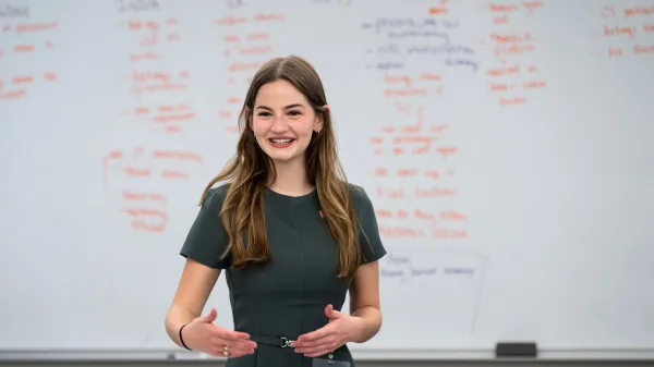 A young woman presents to a class in front of a full board of information