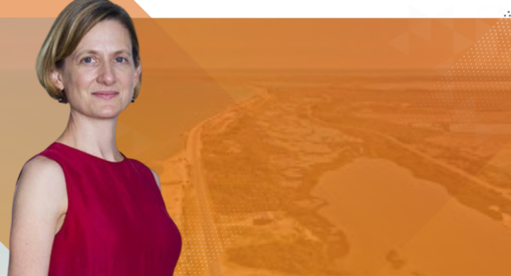 Headshot of Sheila Olmstead with burnt orange background and faded coastline in background