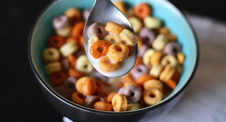 A bowl of cereal loops with some sitting on a spoon.