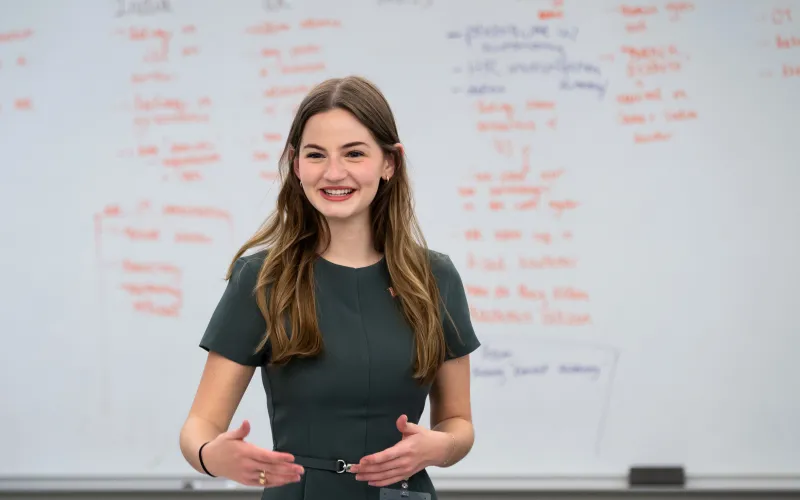 A young woman presents to a class in front of a full board of information